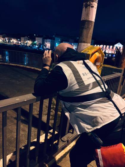 A volunteer scanning the river with binoculars at night