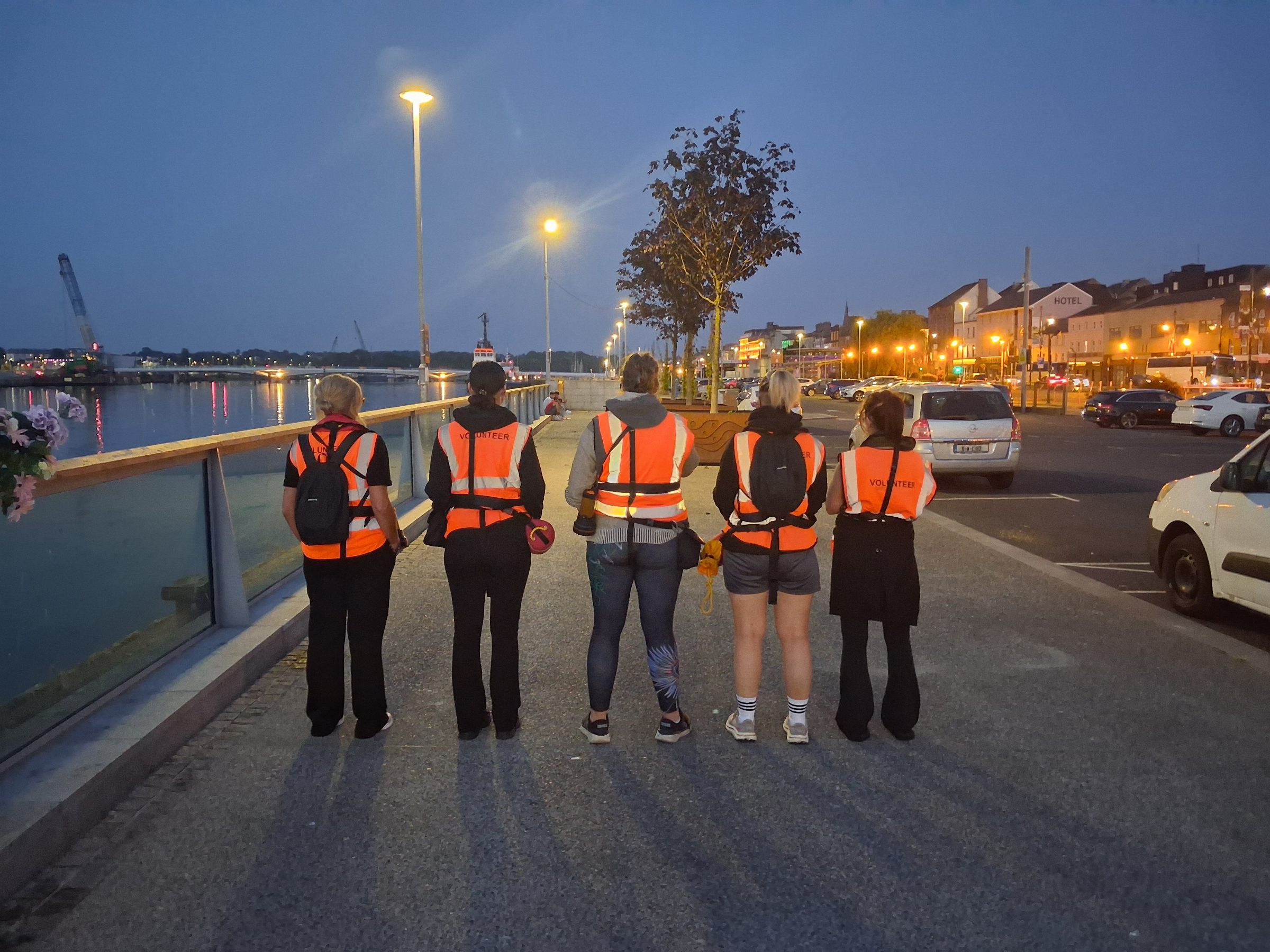 Five Re-A-Suir volunteers in hi-vis vests looking out over the River Suir from Waterford quay at dusk