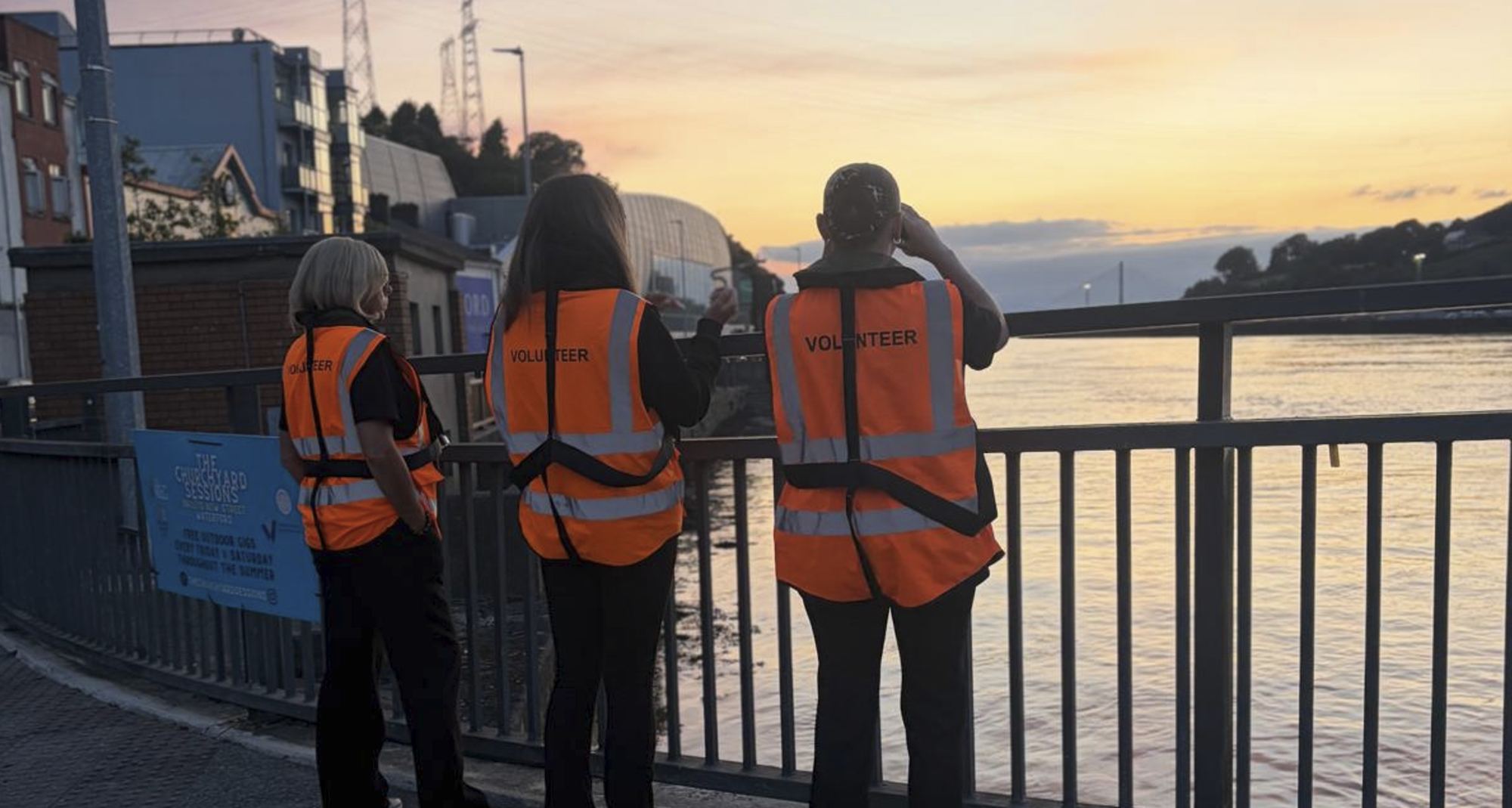Three volunteers keeping watch over the river from the quay at sunset